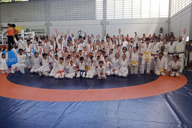 Dezenas de alunos de karatê, crianças e adultos, reunidos sobre o tatame na reinauguração do Centro Olímpico Thomaz Mazzone